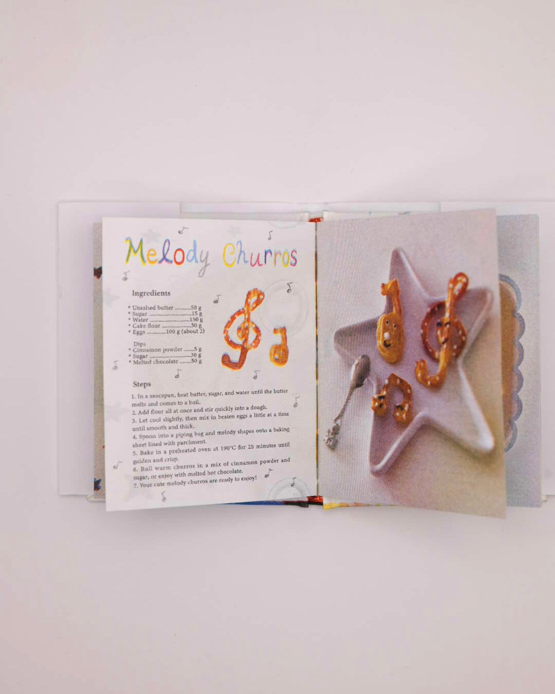 A square art print featuring a whimsical illustration of a cartoon character in a chef hat mixing batter, with the text 'Cooking with Happy' above, shown against a light gray background.